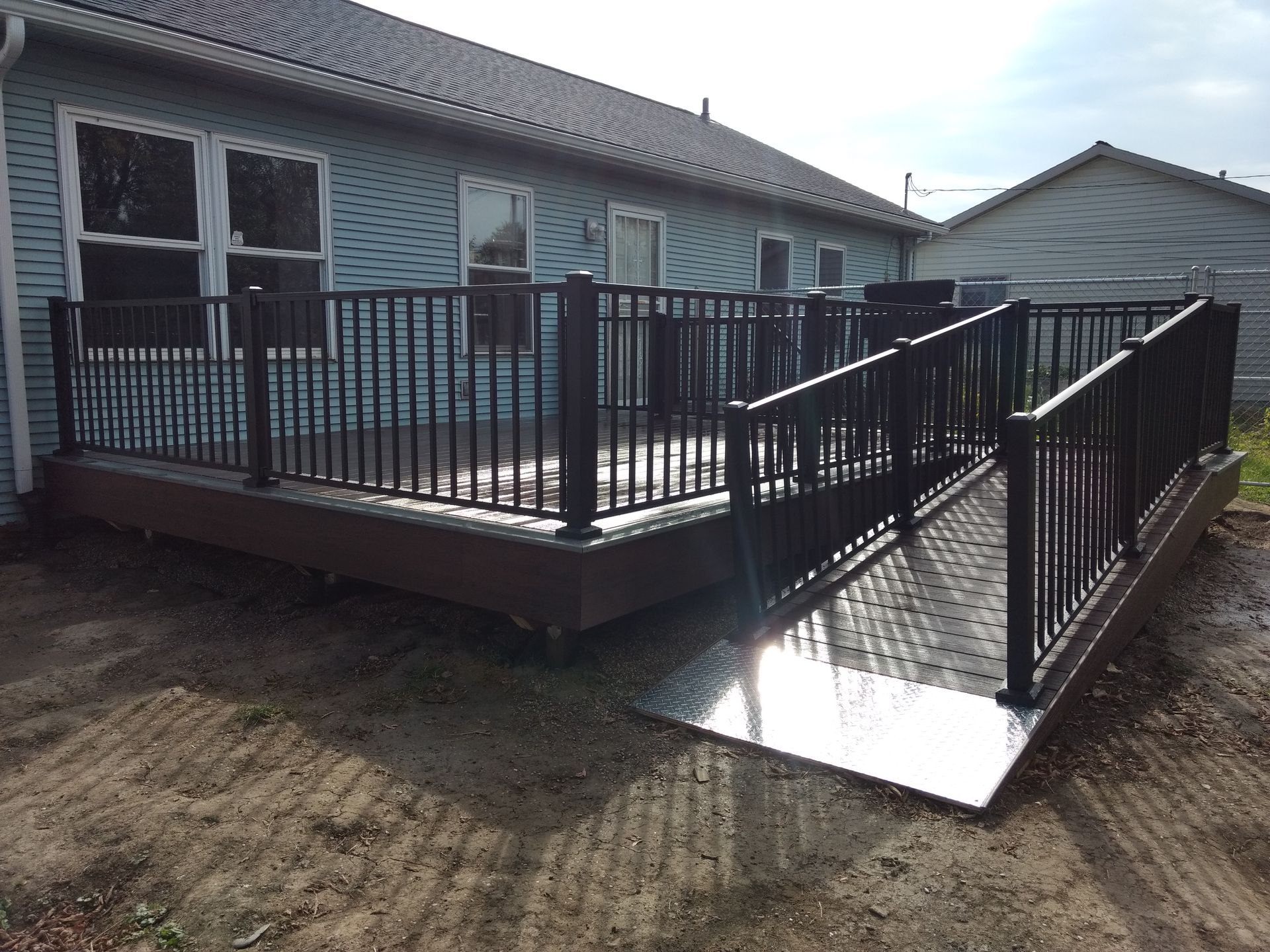 Black deck and ramp attached to a light blue house. Black railing surrounds the deck and ramp.