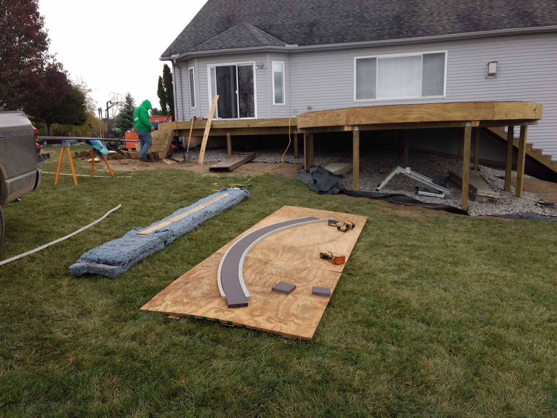 Construction site; deck being built on a lawn. Materials and tools are scattered around. A person is working.