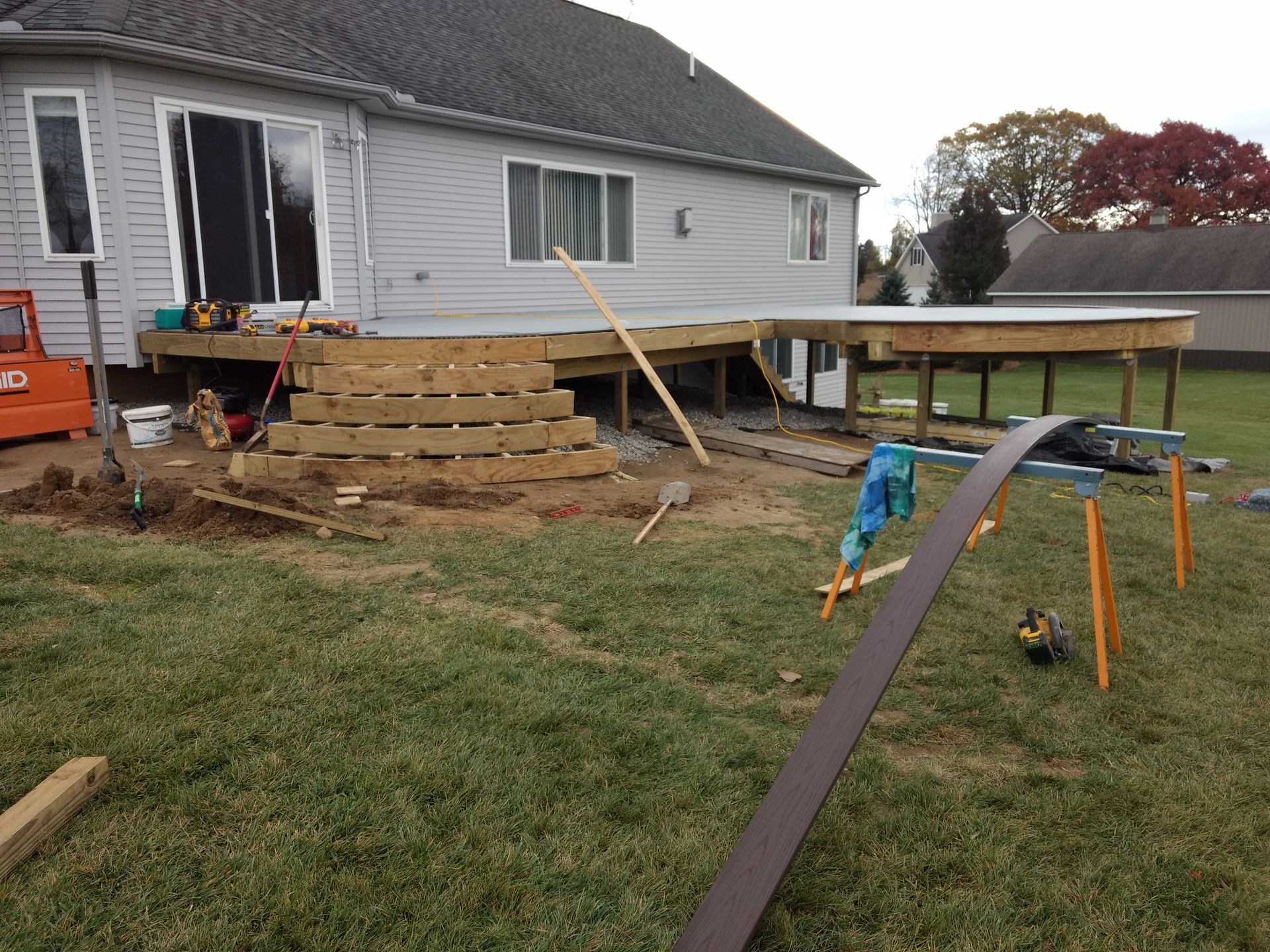 Deck construction in progress; wooden stairs, partial deck, yard, house.