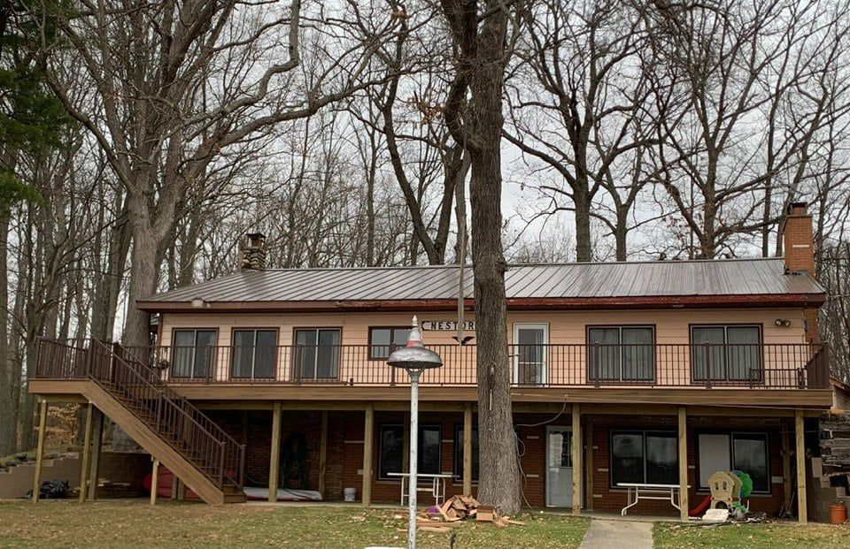 Two-story home with a brown deck and a metal roof surrounded by bare trees.