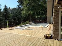 Wooden deck surrounding a rectangular pool under construction, with a forested background.