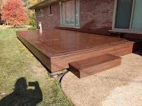 Wooden deck with steps next to a brick building on a sunny day.
