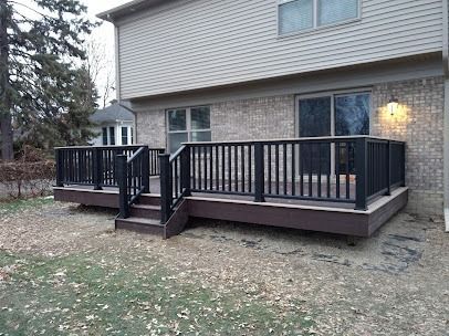 Deck with black railing, brown steps, and composite decking. Attached to a brick and siding home.