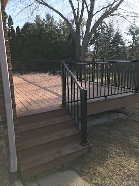 Brown wooden deck with steps, black railing, and a backyard setting.