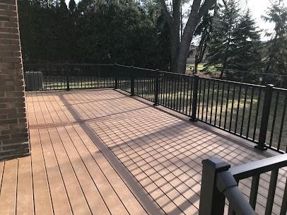 Wooden deck with black railings. Trees in the background. Sunny day.