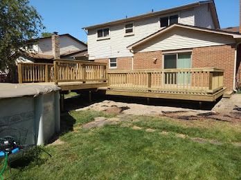 Wooden decks attached to a two-story brick house with a green lawn.