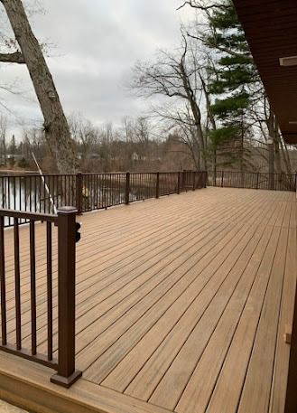 Wooden deck overlooking a calm body of water, brown railings, trees in background, overcast sky.