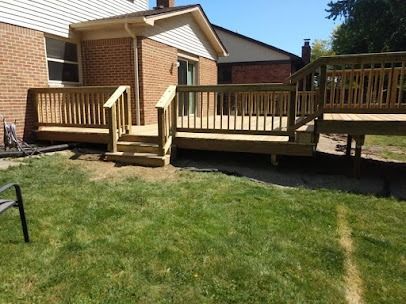 Wooden deck with railings, steps, and access to a yard with green grass. House in background.