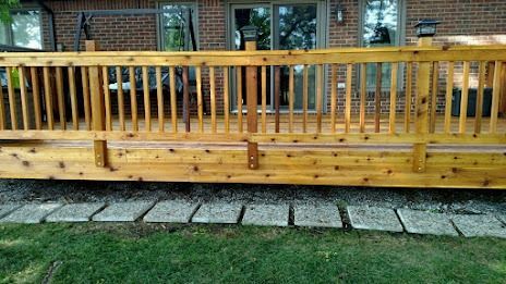 Wooden deck with railing, ground-level brick patio, and green grass.
