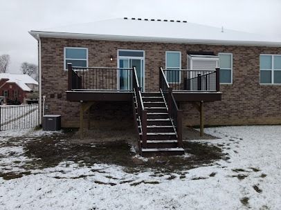 Back of a brick house with a wooden deck and stairs covered in snow.
