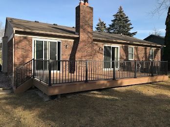 A brick house with a wooden deck and black railing. Two sliding glass doors and a chimney are visible.