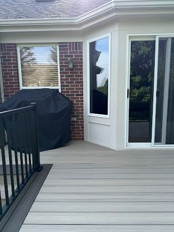 A composite deck with a brick wall, covered grill, and glass door/window.