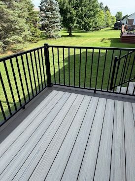 A deck with gray composite boards, black railing, overlooking a green lawn with trees.