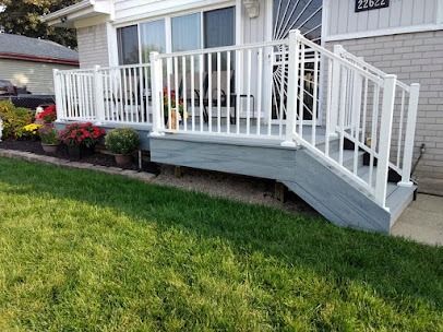 White-railed front porch with gray decking and steps. Green lawn and potted flowers in front.