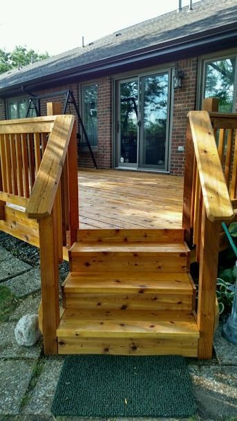 Wooden deck and stairs leading up to sliding glass doors on a brick house.