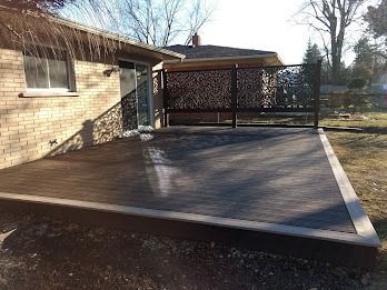 A wooden deck next to a brick building. Dark gray deck, light gray border, decorative fence.