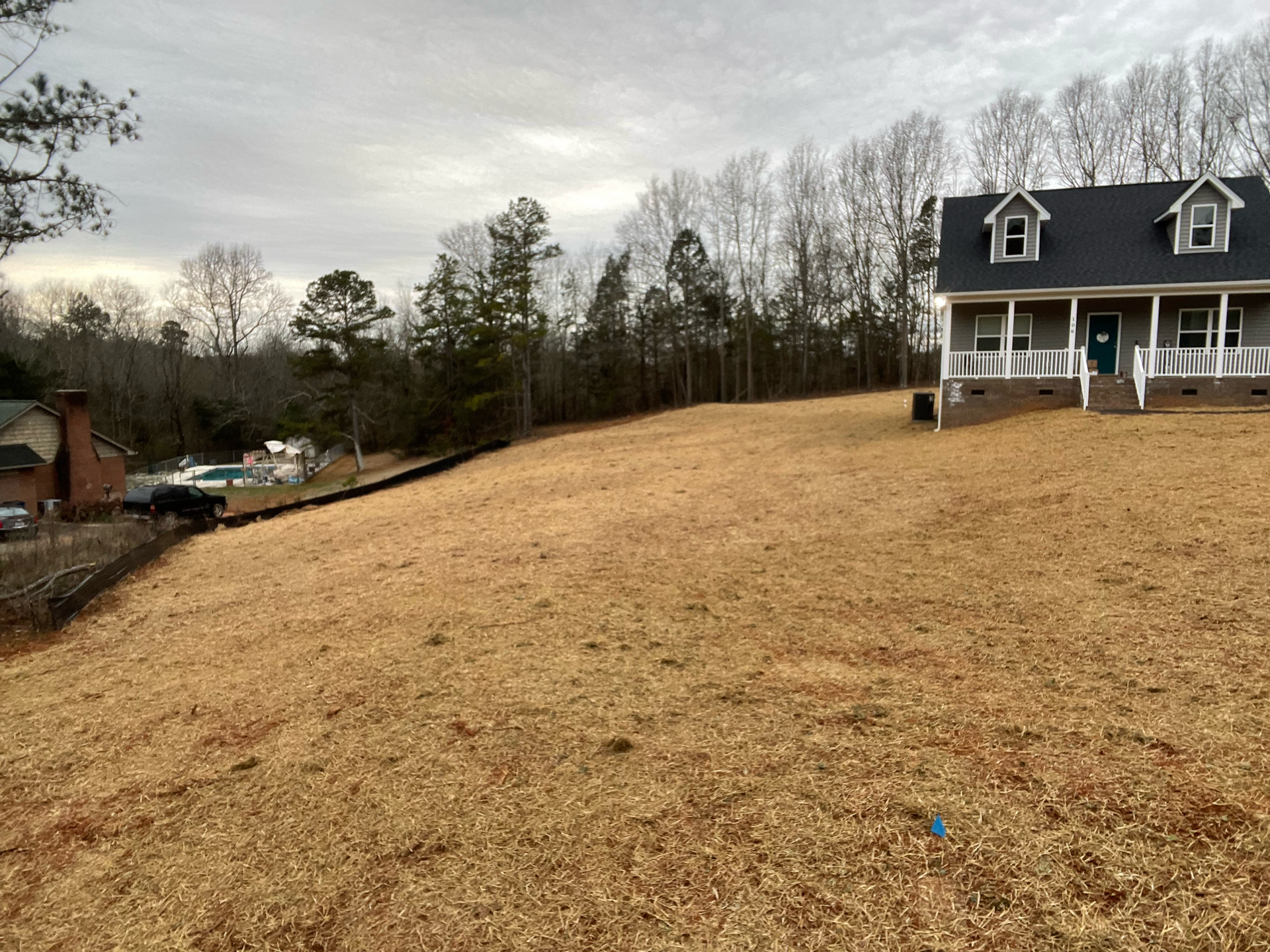A house with a large, bare yard on a cloudy day. Trees in the background.
