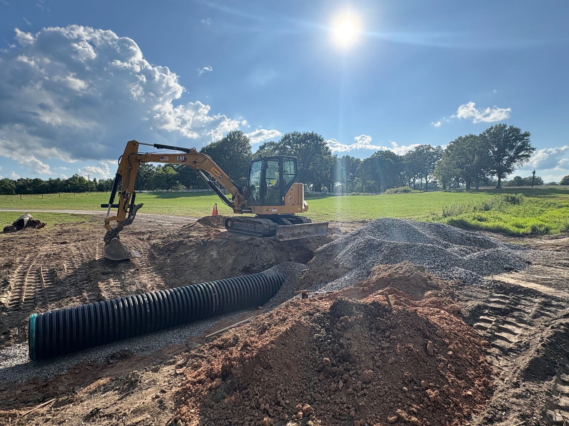 Aerial view of a construction site with yellow excavator and several dump trucks in a dirt area.