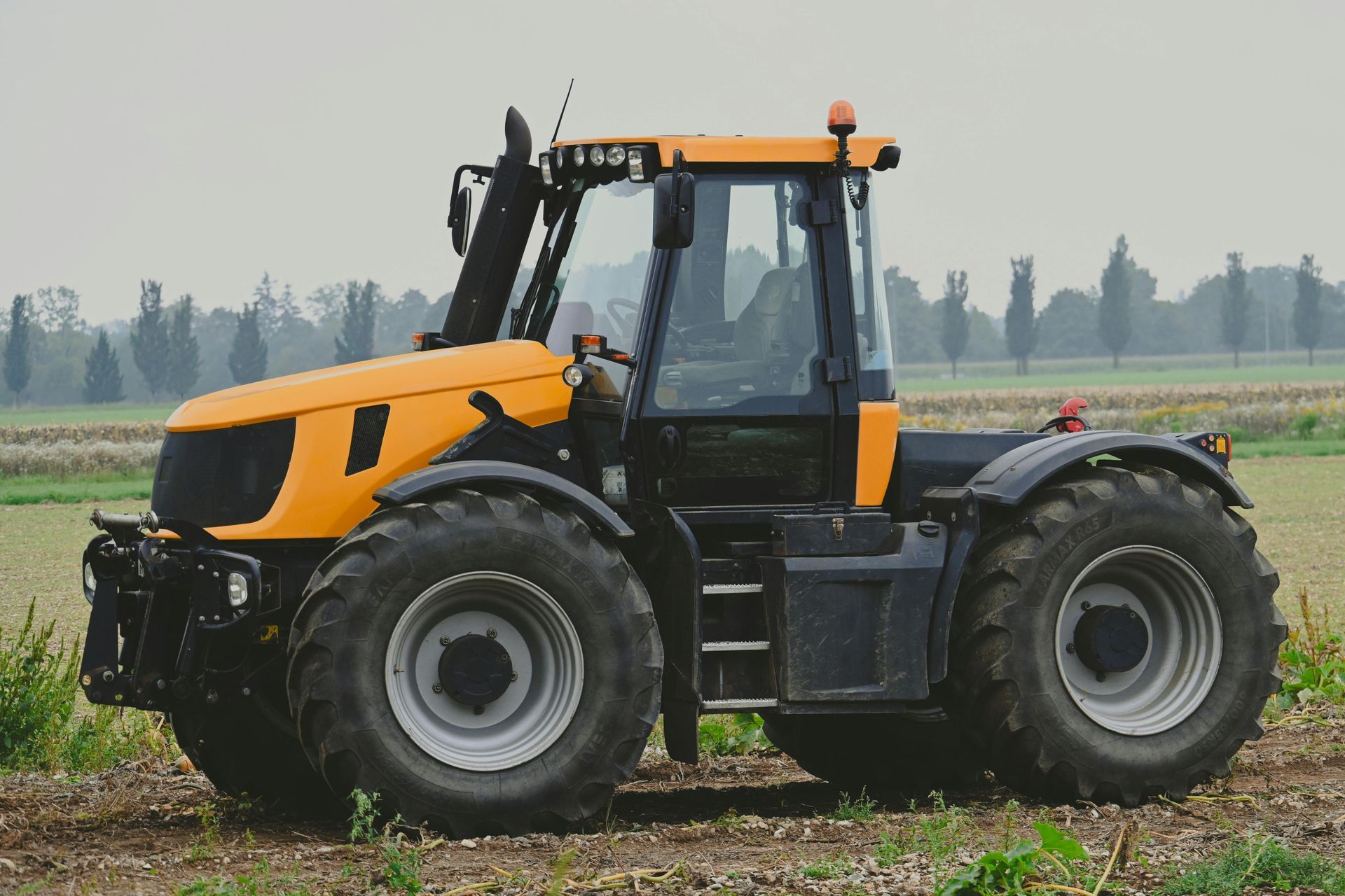 Yellow and black tractor in a field, with large tires and a clear cab.