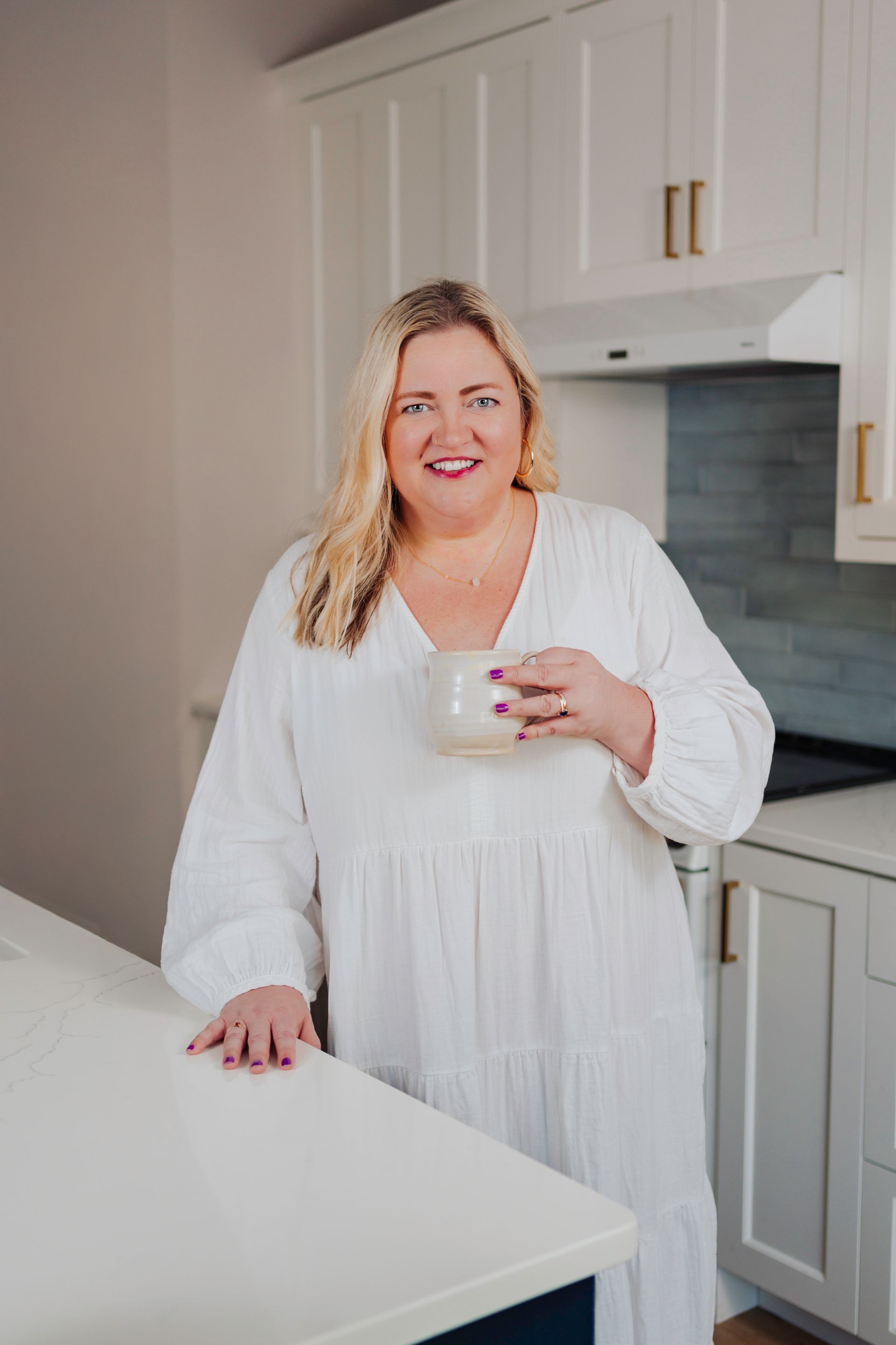 Erin Leigh Patterson smiles at the camera from her kitchen while drinking a cup of coffee