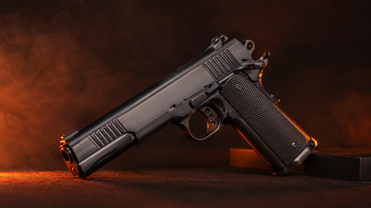 Black handgun on a dark surface with orange backlighting and smoke-like glow.