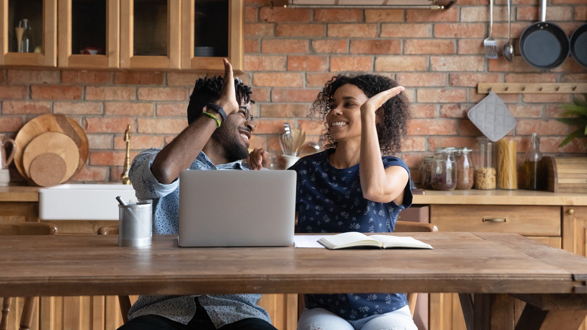 Two smiling people sitting together at a desk high-five to indicate success.