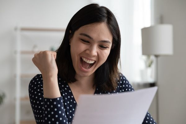 A woman with brown hair looks joyfully at a piece of paper, indicating success with her medical billing issue. Her fist is raised and her mouth is open.