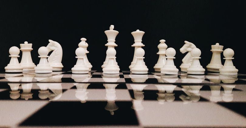 A row of white chess pieces on a black and white chess board