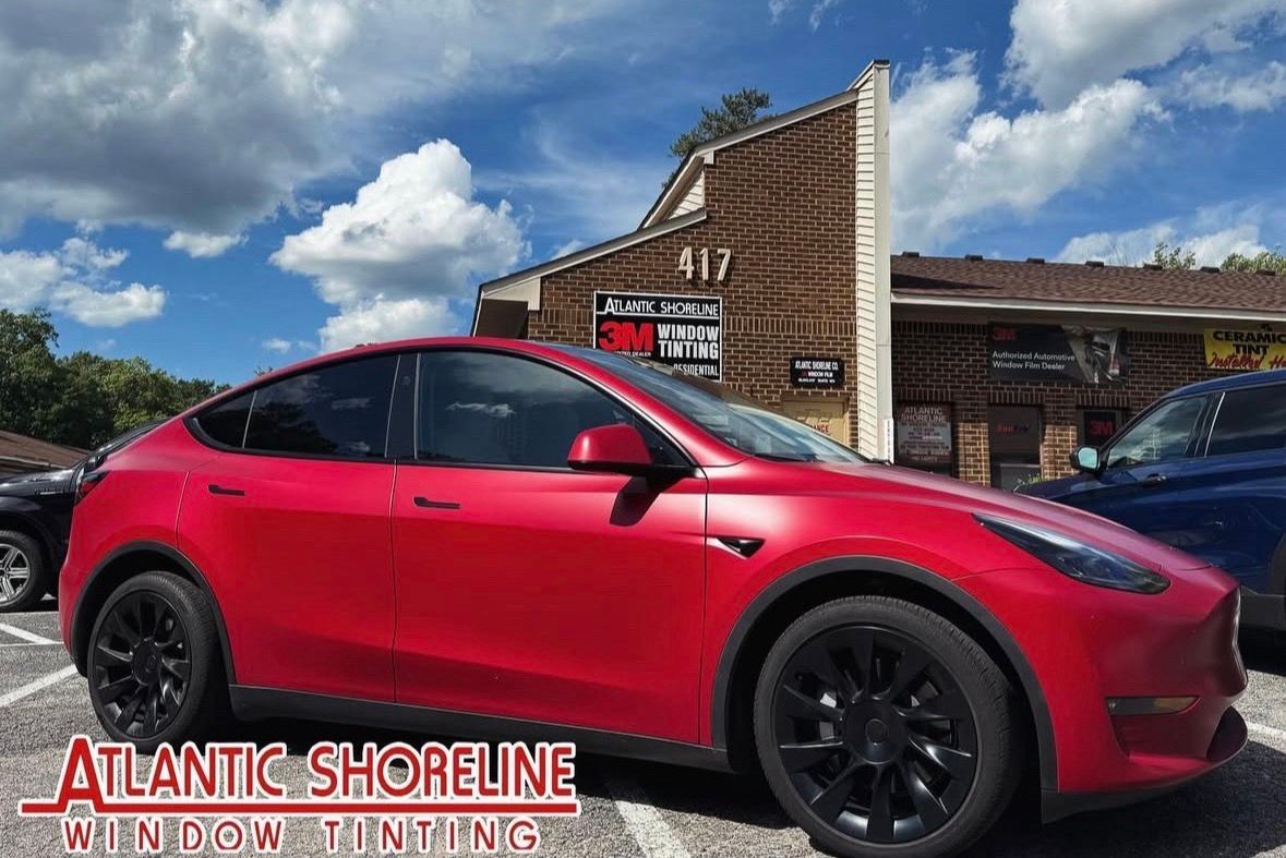 Red Tesla Model Y with black wheels parked near a building with the address "917". Sky with clouds.