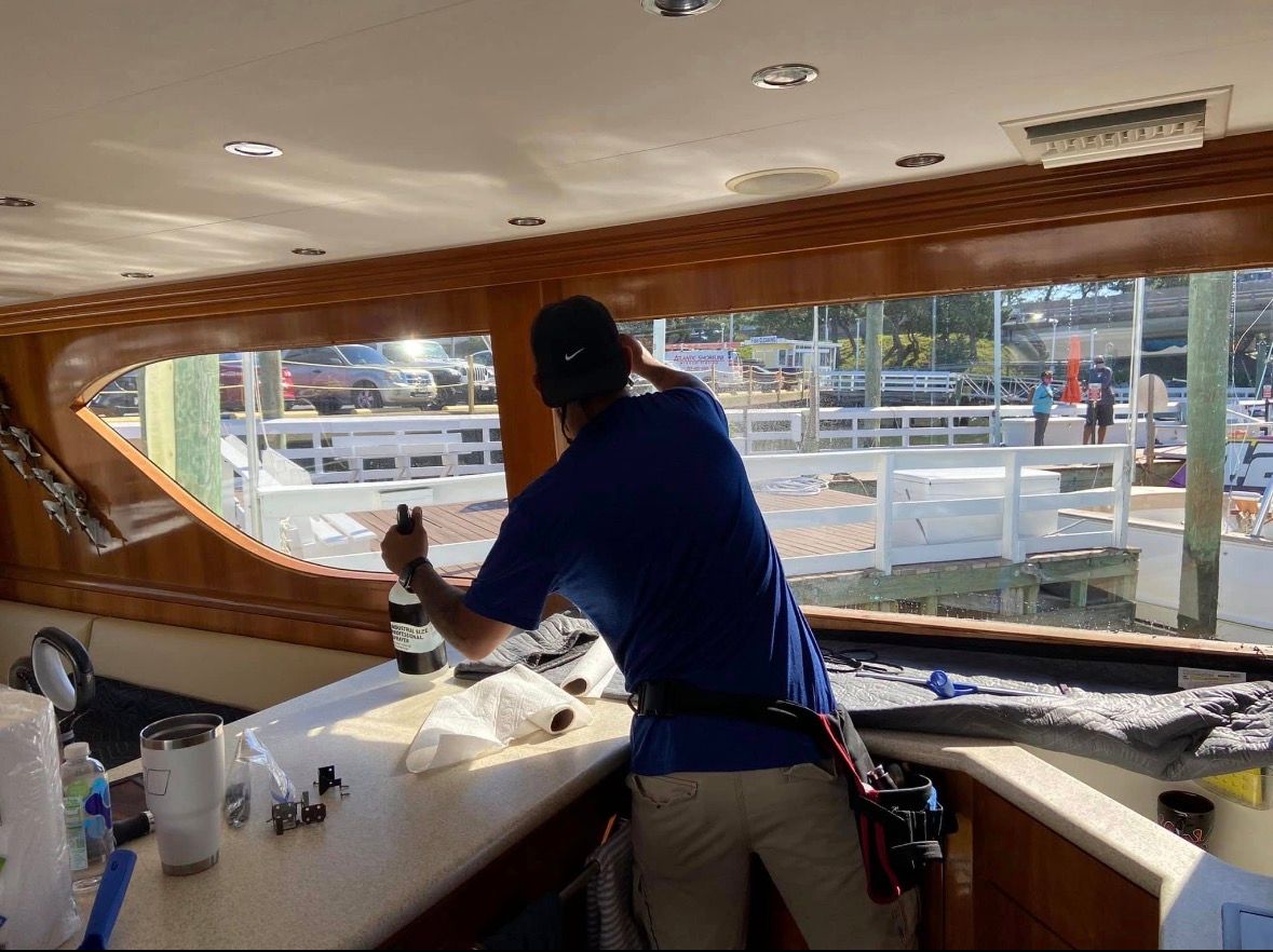 Man applying film to boat window, harbor view in background.