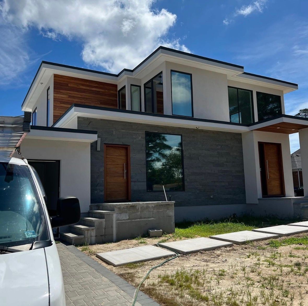 Modern two-story house with gray stone accents and wood doors on a sunny day.