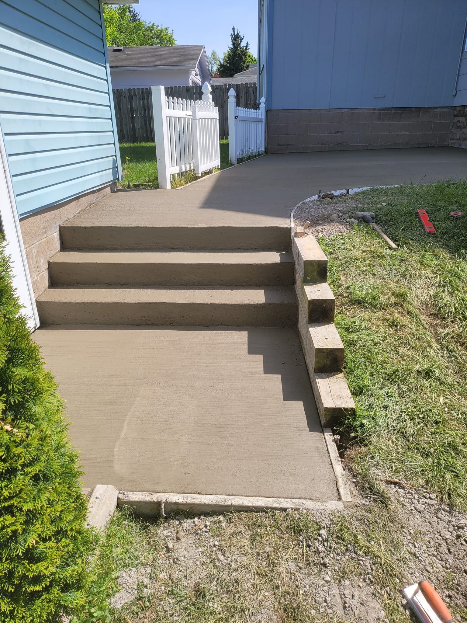 Concrete patio with pool, brown umbrella, picnic table, and fence in backyard.