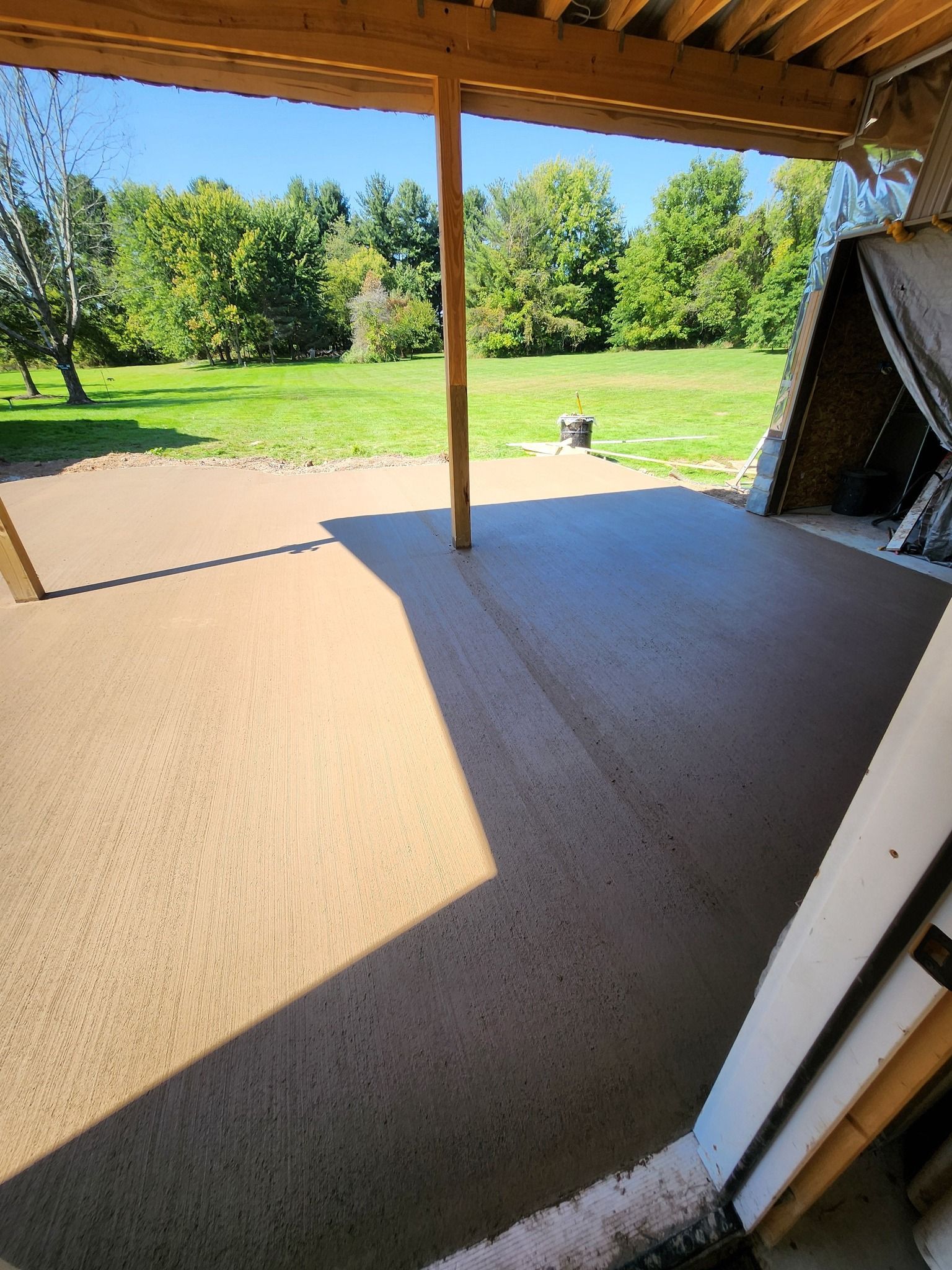 Concrete patio with pool, brown umbrella, picnic table, and fence in backyard.