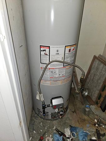 A water heater is sitting in a messy room next to a door.