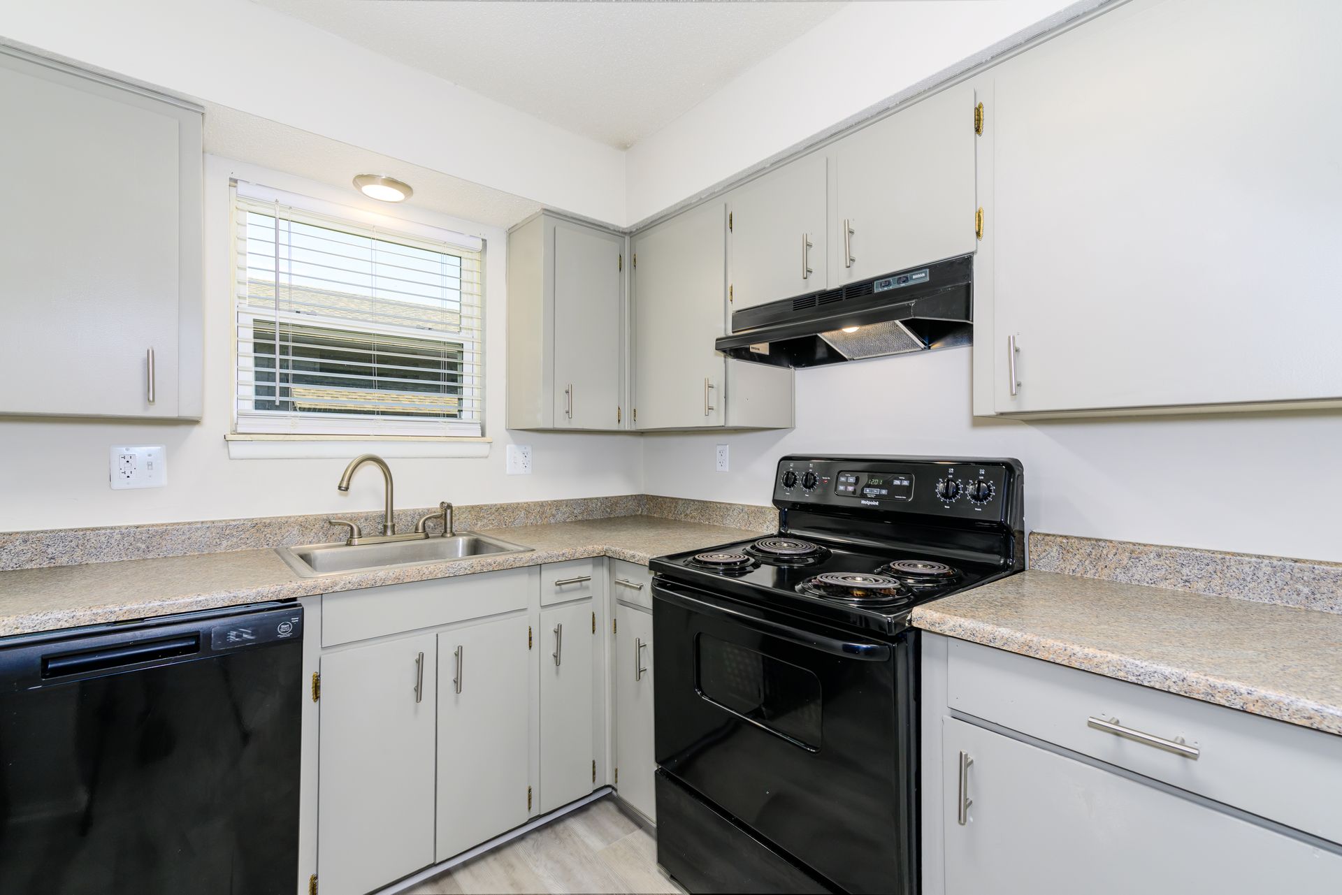 A kitchen with white cabinets , black appliances , a sink and a window.