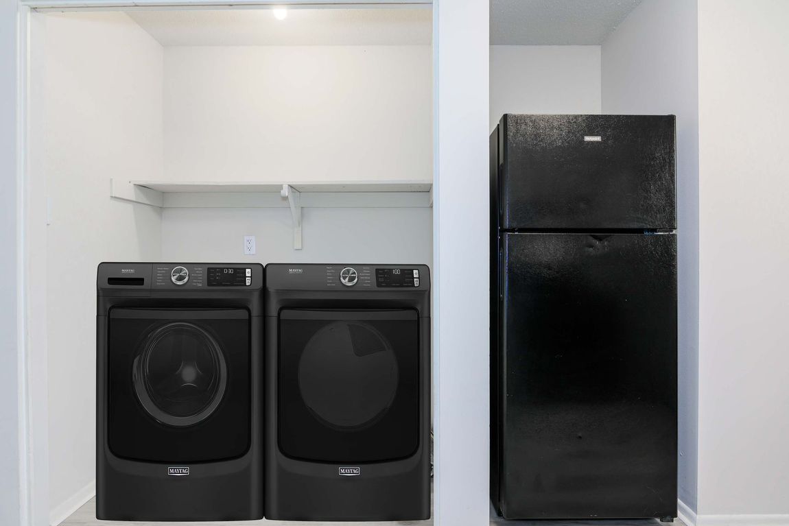 A laundry room with a washer and dryer and a black refrigerator.