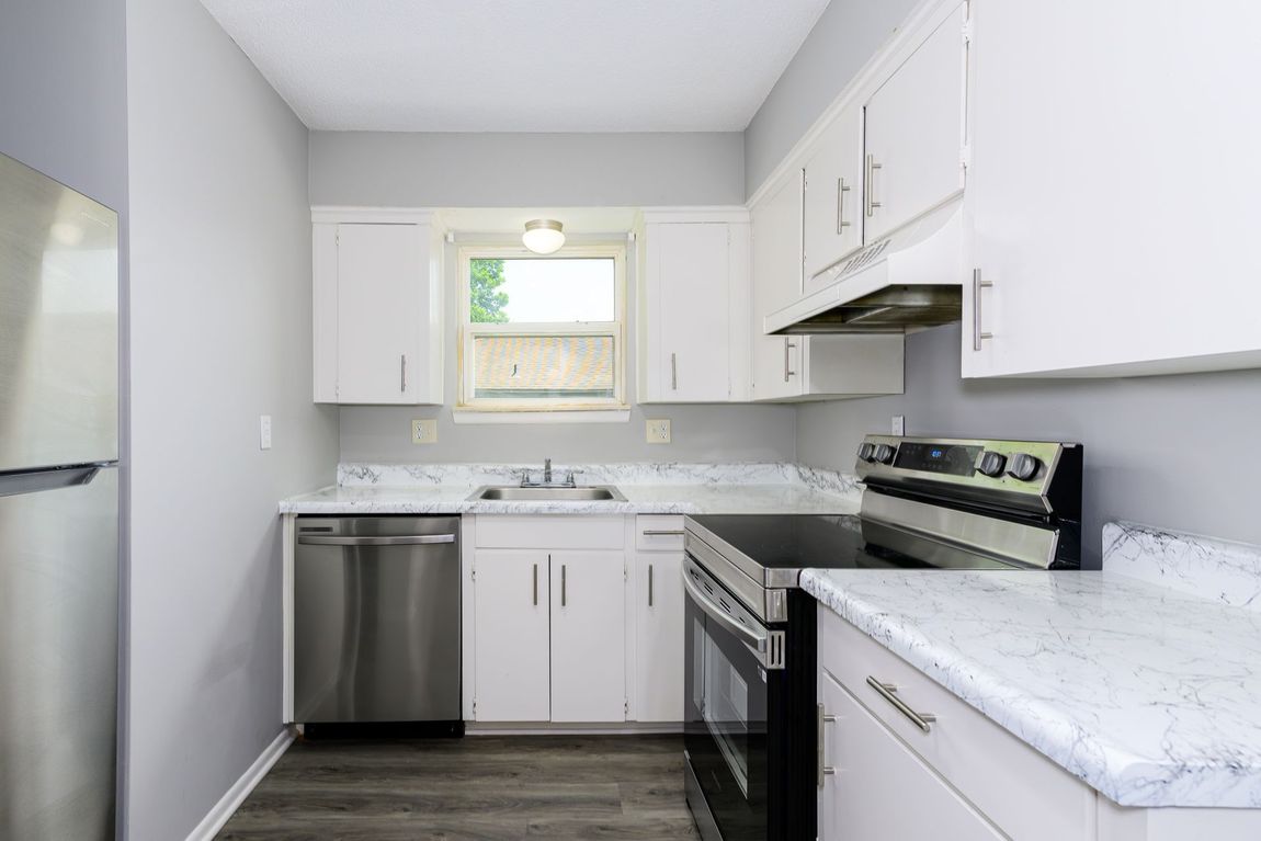 A kitchen with white cabinets , stainless steel appliances , a refrigerator and a dishwasher.