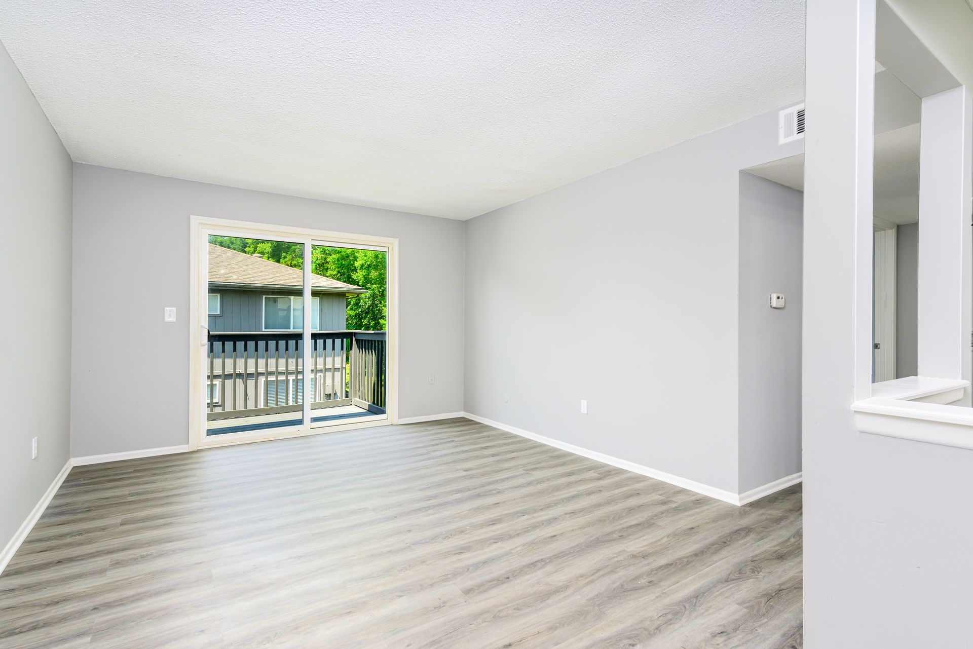 An empty living room with a balcony and sliding glass doors.