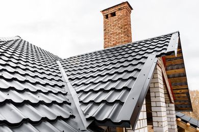 The metal shingle roof of a house with a chimney on it.