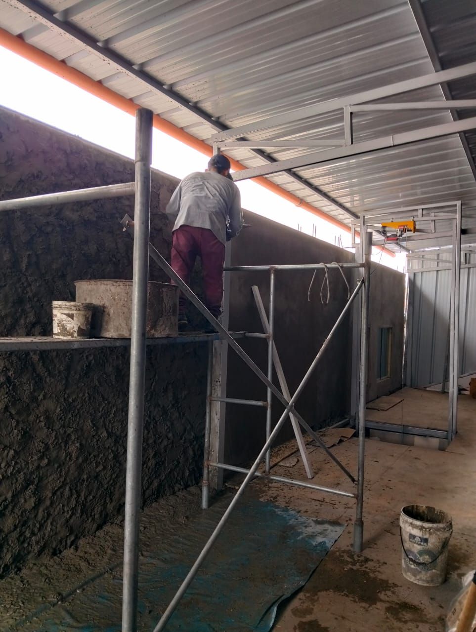 Una persona de pie sobre un andamio pinta una pared bajo una pasarela cubierta.