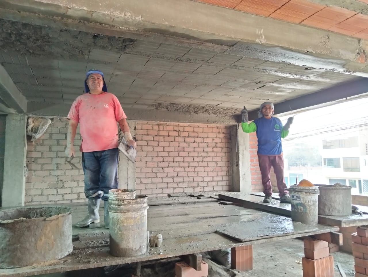 Dos trabajadores de pie sobre una losa de hormigón en construcción con cubos y herramientas cerca