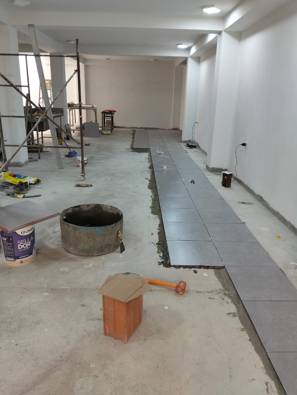 Interior sin terminar con suelo de hormigón, azulejos en las paredes, andamios y herramientas de construcción.