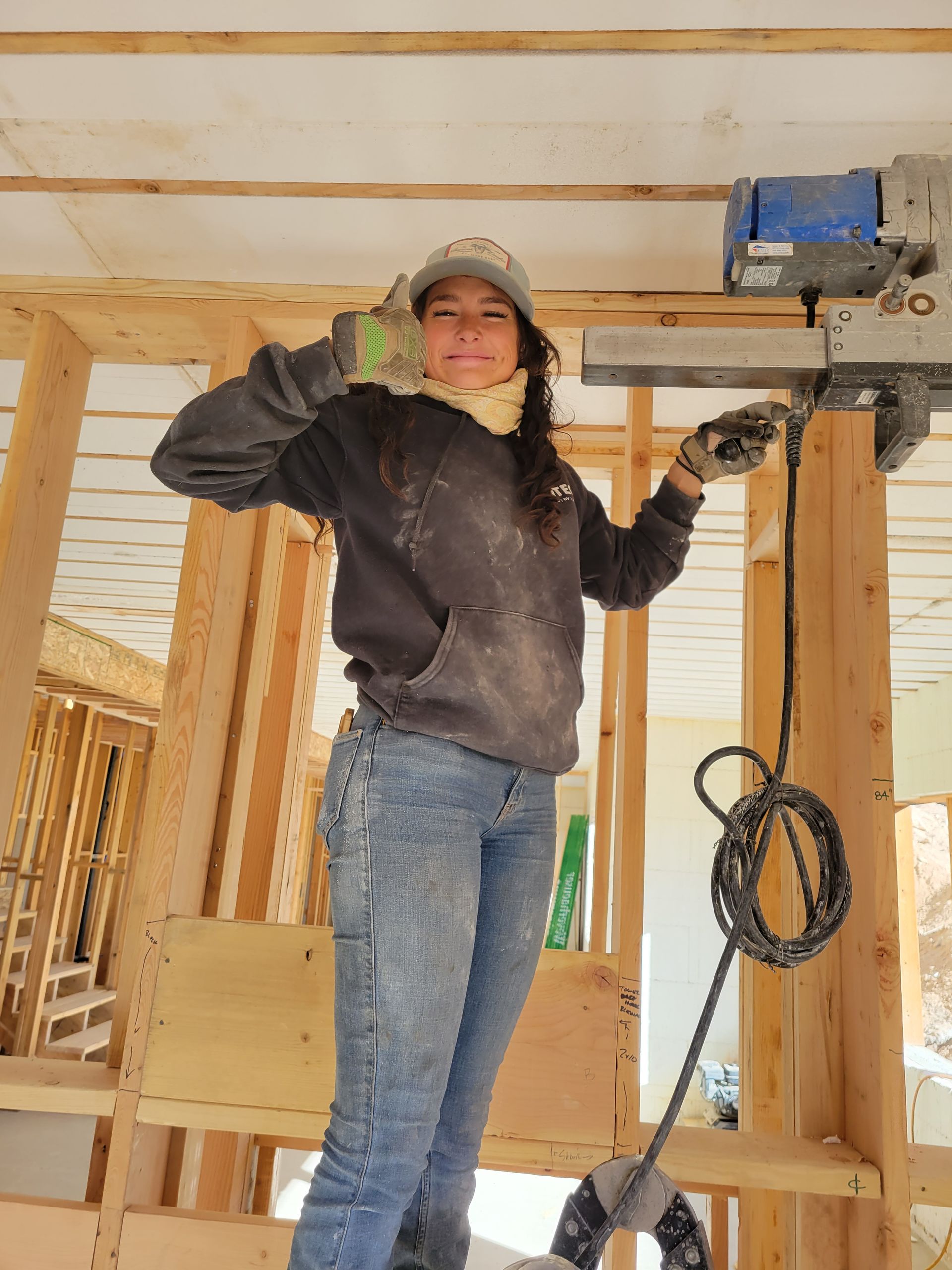 A woman is standing in a building under construction holding a machine.