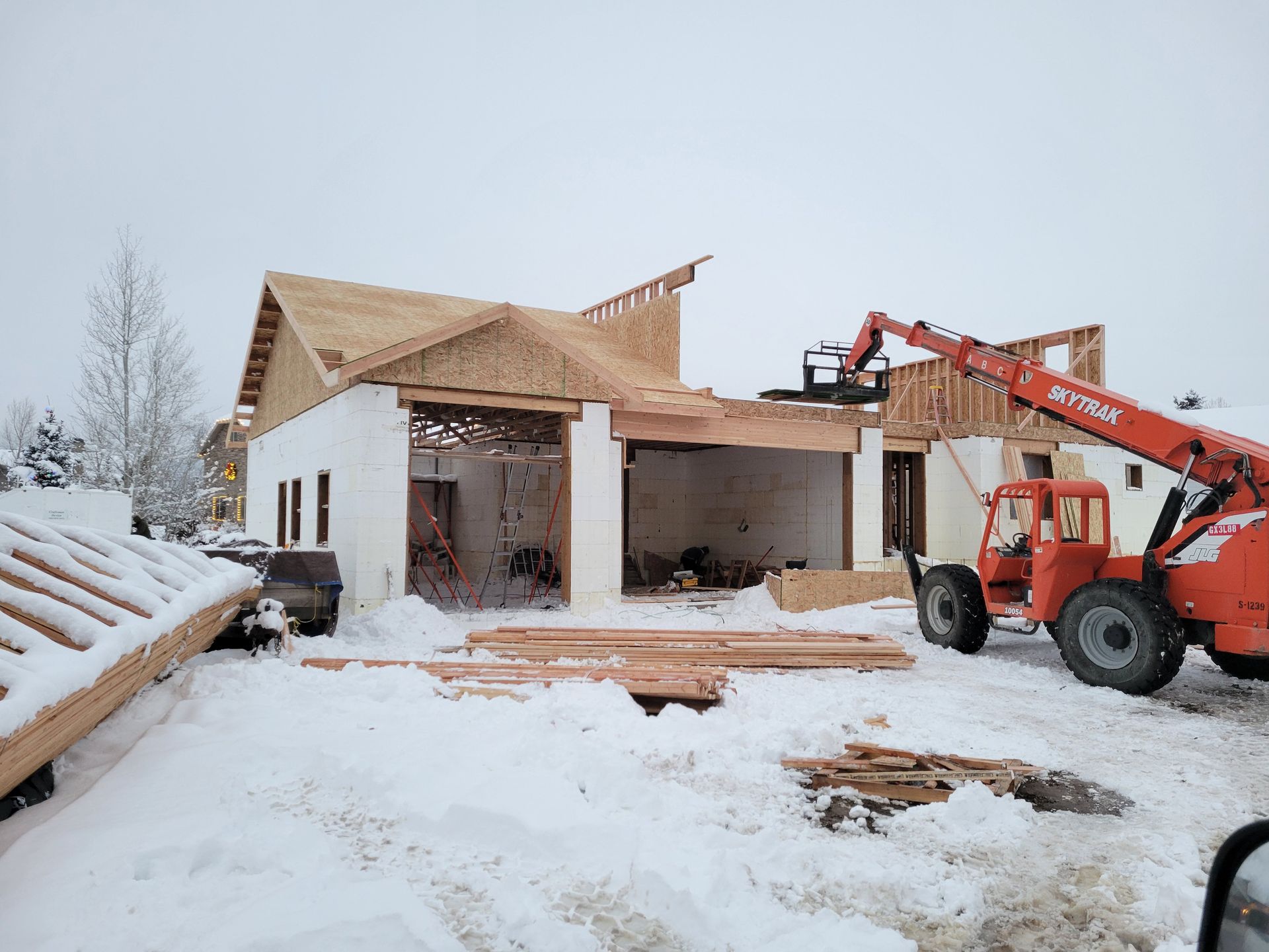 A house is being built in the snow with a forklift in front of it.