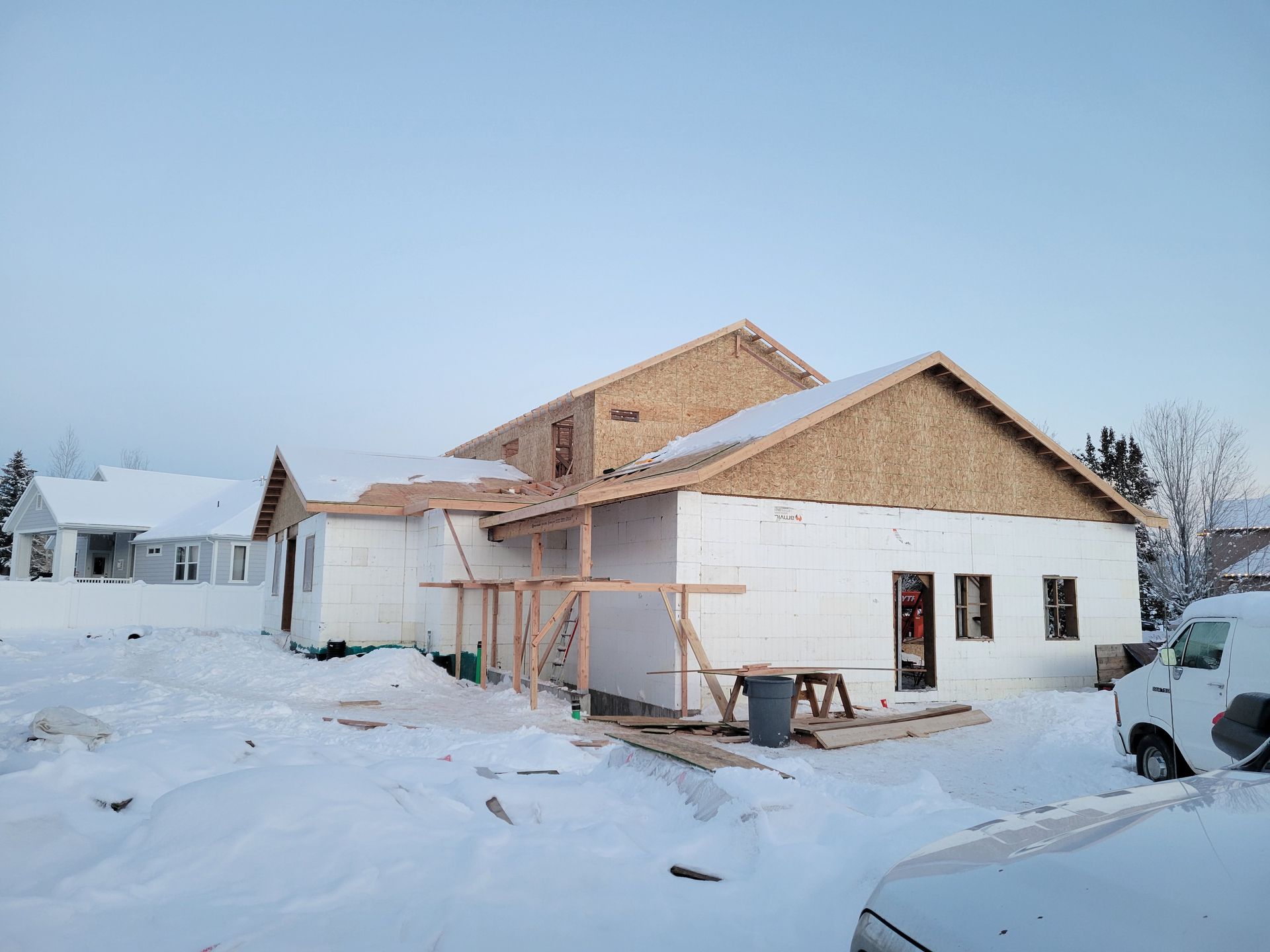A house is being built in the snow with a truck parked in front of it.