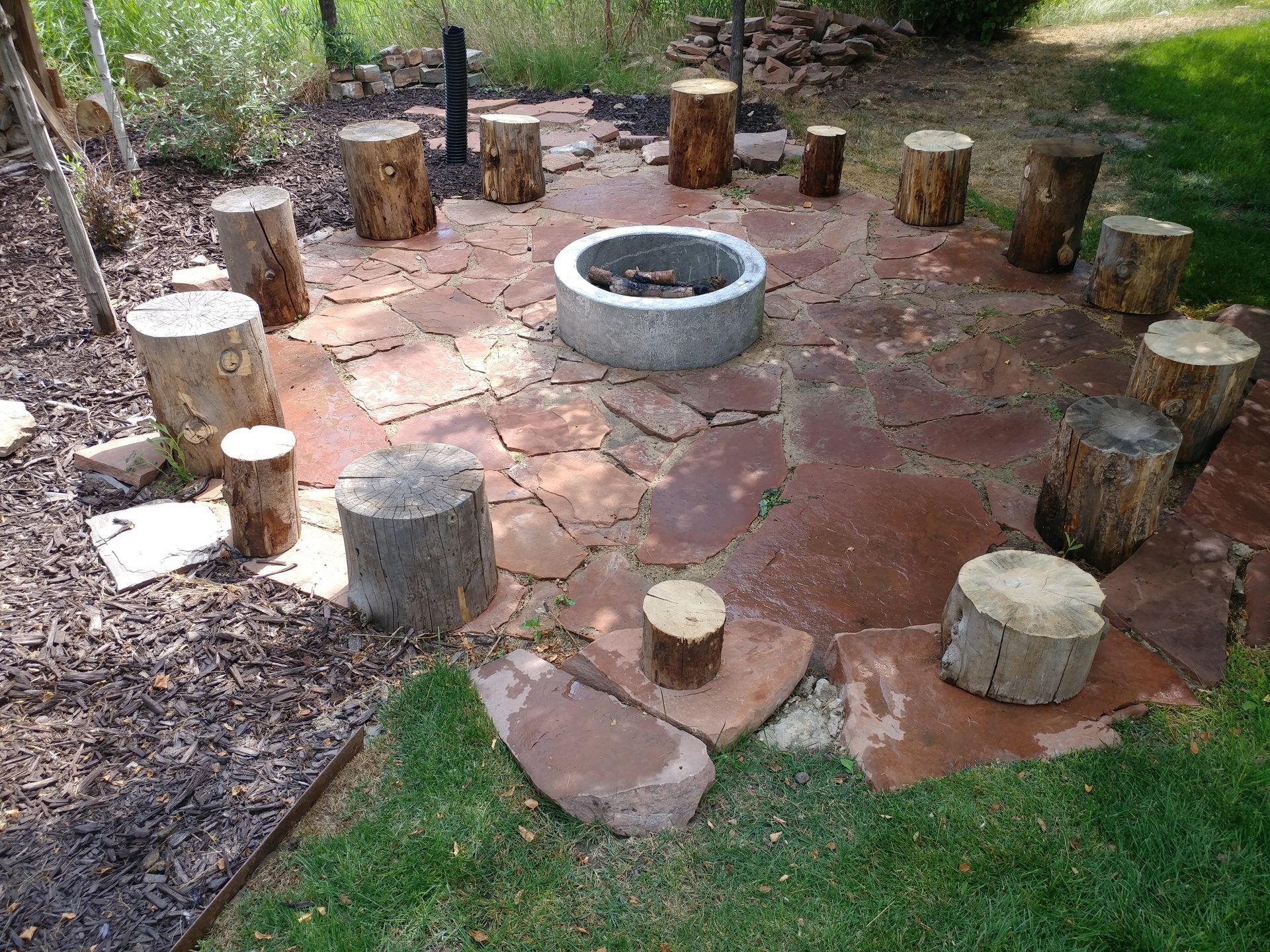 A fire pit surrounded by logs and rocks in a backyard.