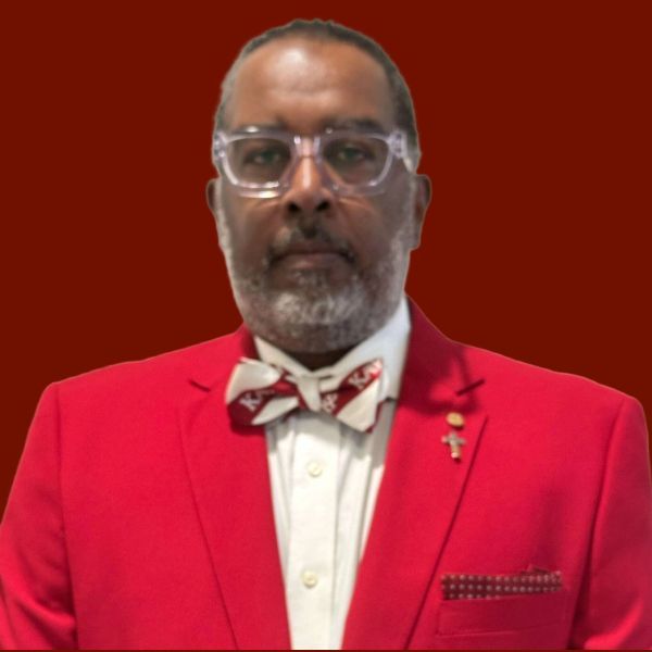 Man in red suit and bow tie, wearing glasses, looking at the viewer.