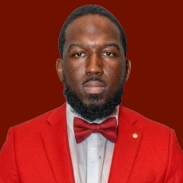 Man in red suit and bow tie, looking directly at the viewer against a red background.