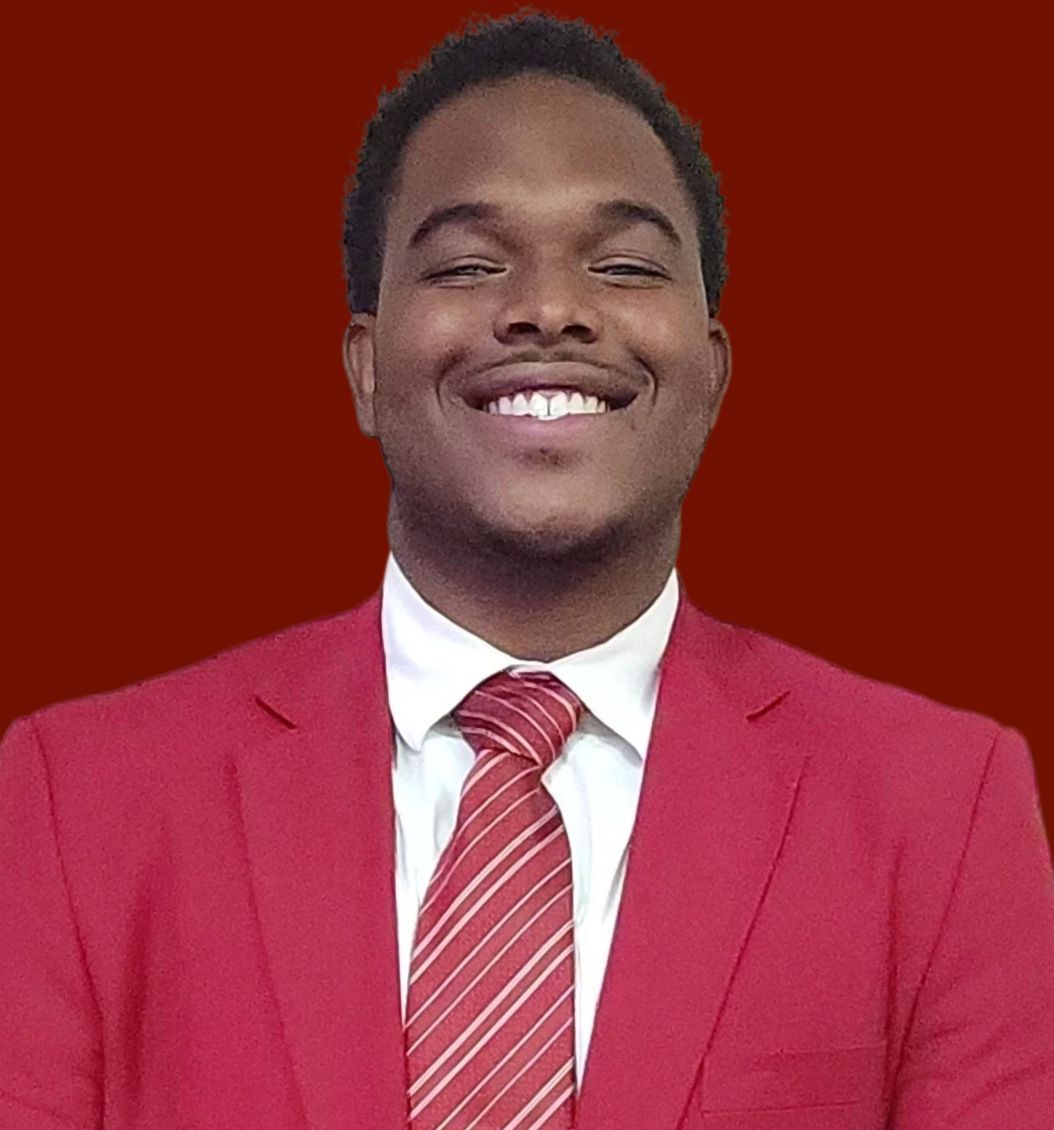 Man in a red suit and tie, smiling broadly against a red background.