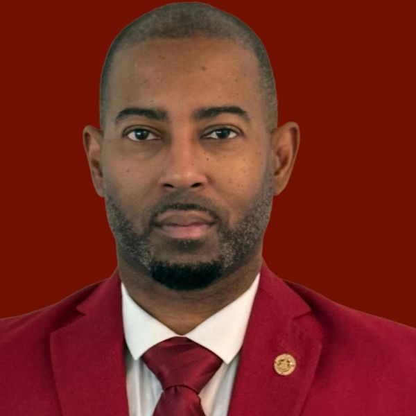 Man in a red suit, white shirt, and red tie, looking directly at the camera with a neutral expression.
